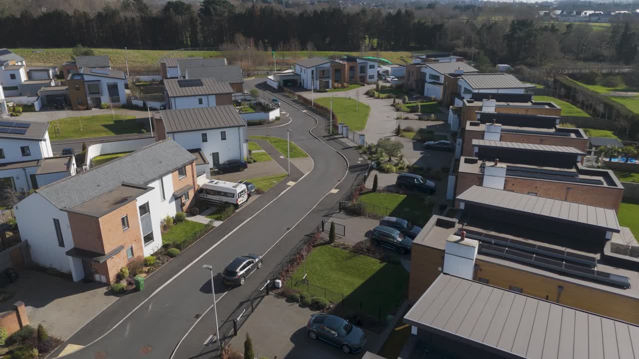Aerial look at white-walled solar-panel homes lining small curved road with uniform hedges and lamp posts indicating new energy-performance build