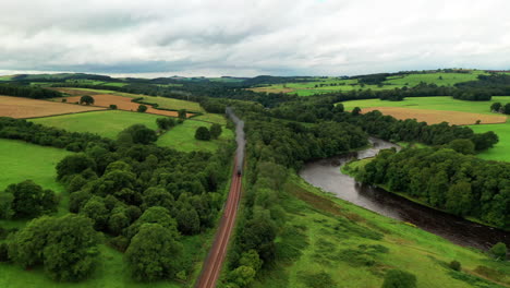 Aerial-dolly-shot-of-a-steam-train-traveling-towards-camera-in-the-rural-countryside,-bright-daylight