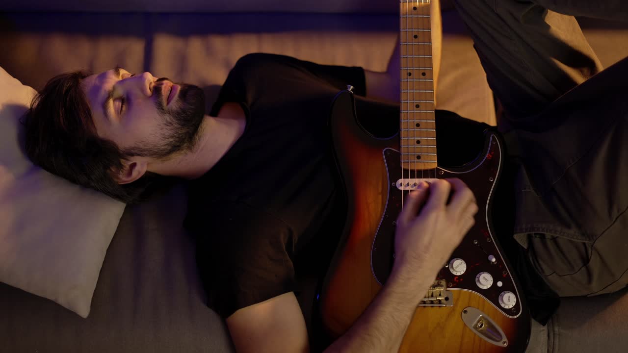 hombre tocando la guitarra mientras está acostado en el sofá con los ojos cerrados