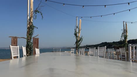 puerta de madera frente al mar y mesa vacía con sillas en la playa para el lugar de celebración