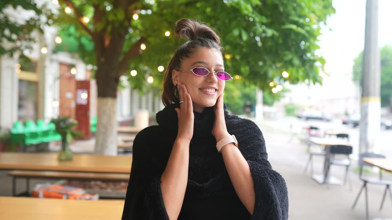 mujer joven con gafas de sol rosas y capa negra al aire libre