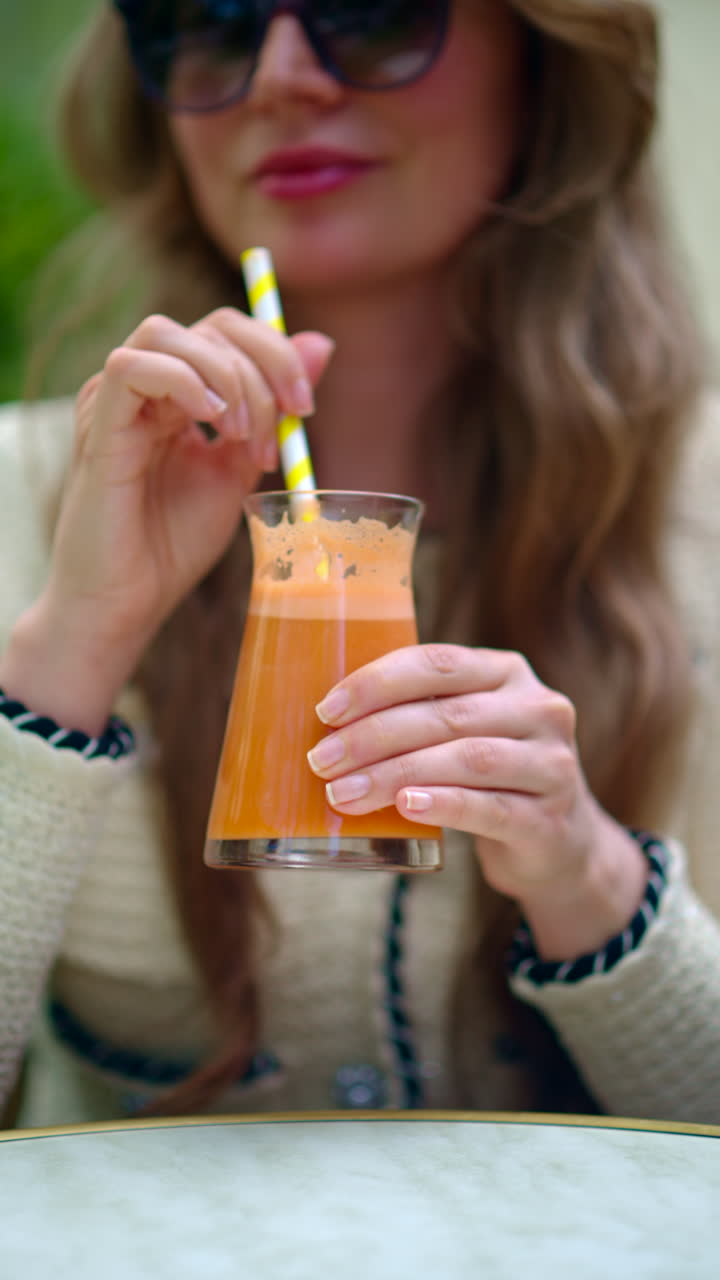 Woman drinking an orange juice using of a straw, at a cafe, outside. Vertical