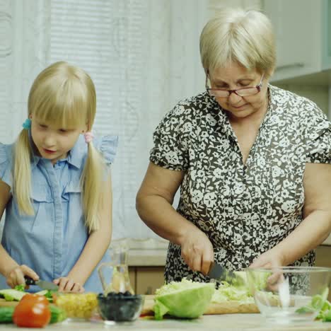 Graciosa-Niña-De-6-Años-Ayuda-A-Su-Abuela-A-Preparar-Comidas-En-La-Cocina-1