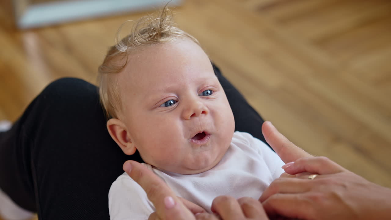 Parents play with their adorable baby. Dad's fingers touch cute plump kid's cheeks. Close up.