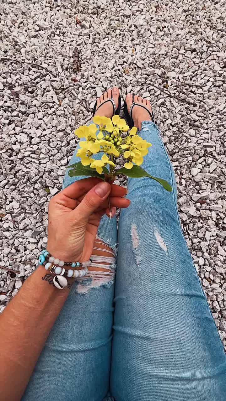 mujer con flores amarillas, con vaqueros y sandalias en el suelo de grava