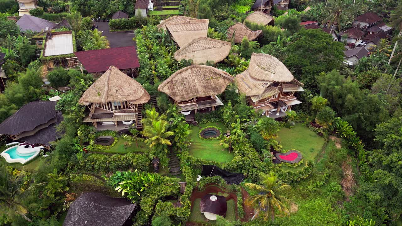 Drone view of bamboo villas in Ubud set on a lush hillside with tropical gardens, serene pools, and handcrafted wooden design, creating a peaceful eco accommodation with scenic valley views