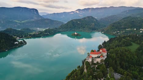 Castillo-Sangrado-En-Roca-Con-Vista-Al-Hermoso-Lago-Sangrado-Eslovenia-Con-Iglesia-En-El-Fondo,-Disparo-De-Drones-De-Paralaje-Aéreo,-Reflexión-Matutina,-4k-Cinematográfico