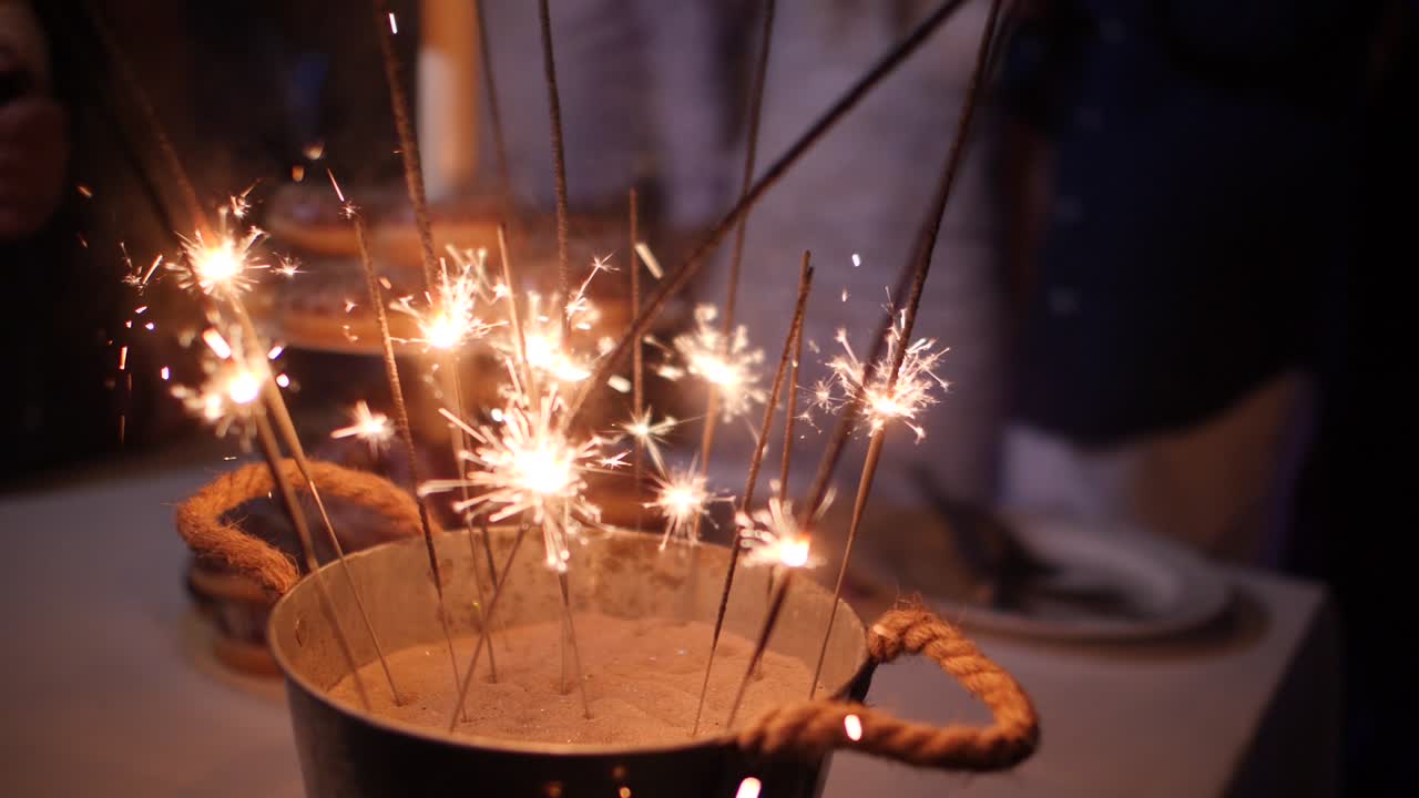 Slowmotion-nærbillede af rustikke dekorationer med mange stjernekastere, der brænder i en sandspand til en bryllupsfest