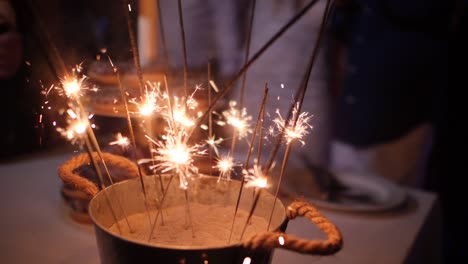 slow motion close-up on rustic decorations with many sparklers burning in a sand bucket at a wedding reception party