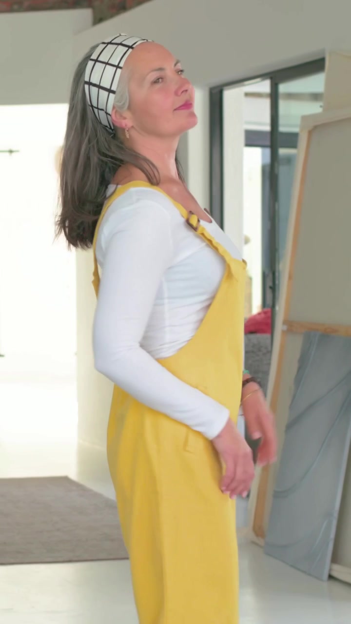 Video verticale: Ingresso nella sala da pranzo, donna in abito giallo che si muove e ispeziona specchio e tele.