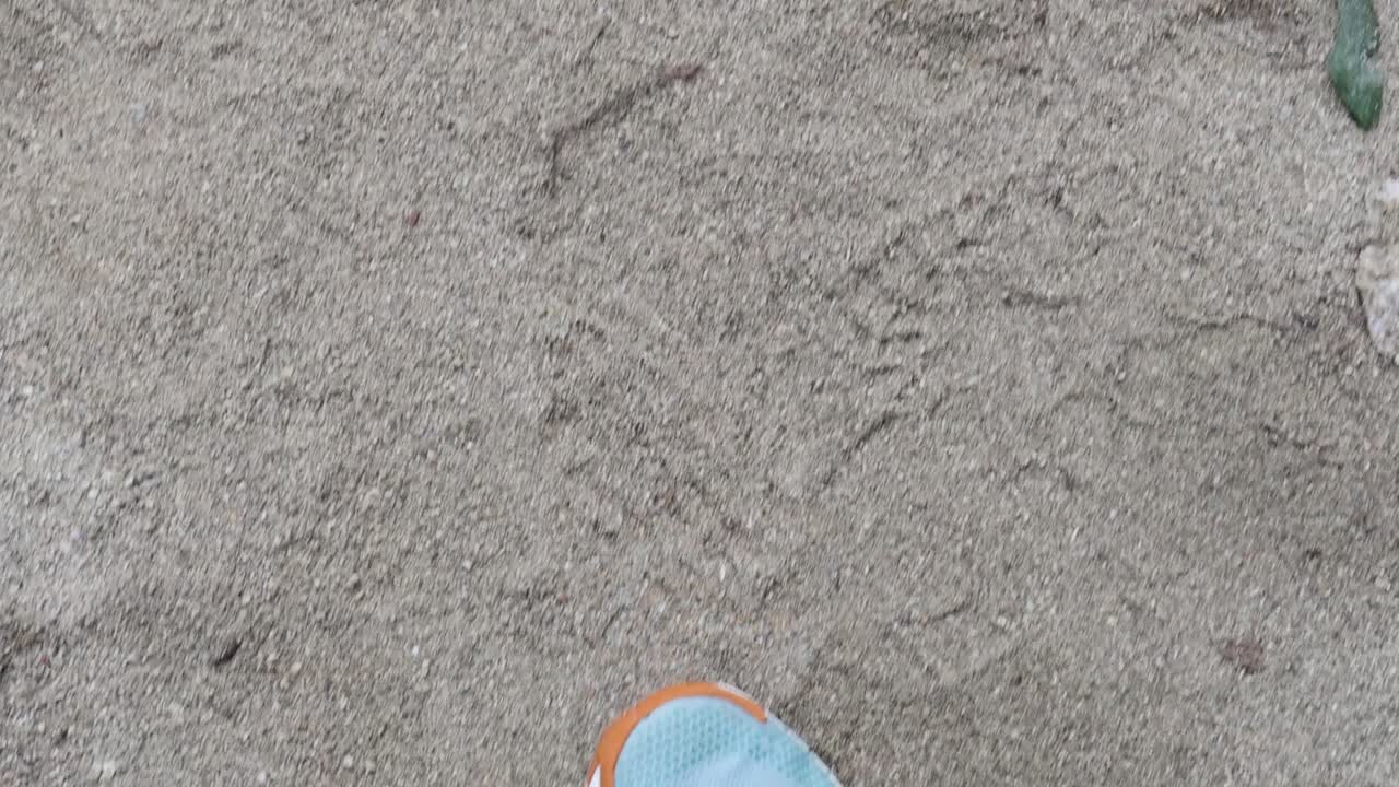 A person walks on sandy terrain in Port Douglas, Queensland. The video captures steady footsteps with bright sneakers