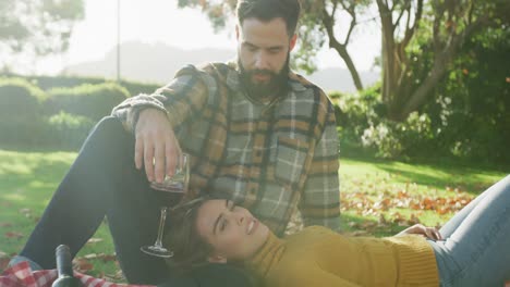 video de una feliz pareja caucásica vestida cálidamente bebiendo vino en el jardín