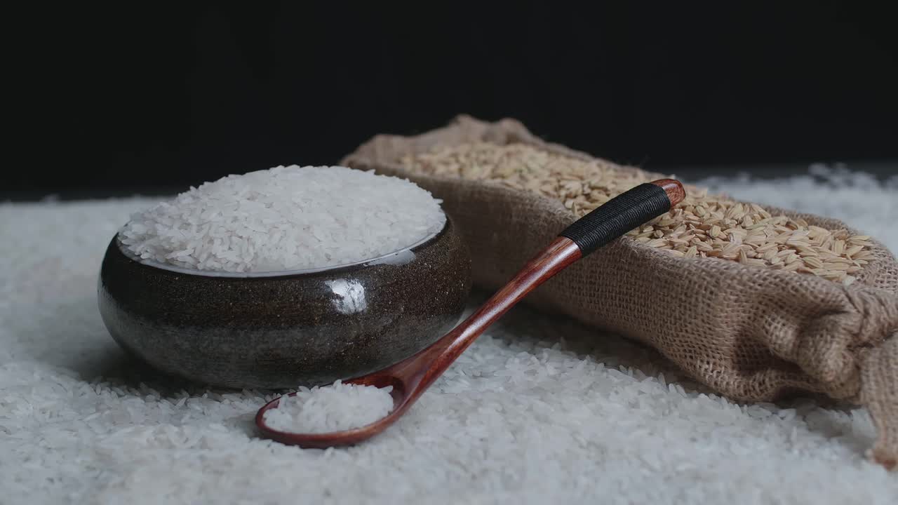 Raw Rice Grain In Unique Bowl, Rustic Bag And Wooden Spoon Rotate In Slow Motion.
