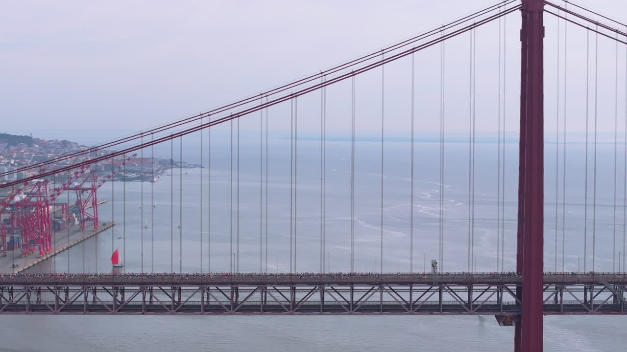 Side-on aerial drone shot of half marathon and 10K long-distance running event in Lisbon, Portugal, Europe. Runners crossing the iconic famous red 25th April suspension bridge, drone flying backwards