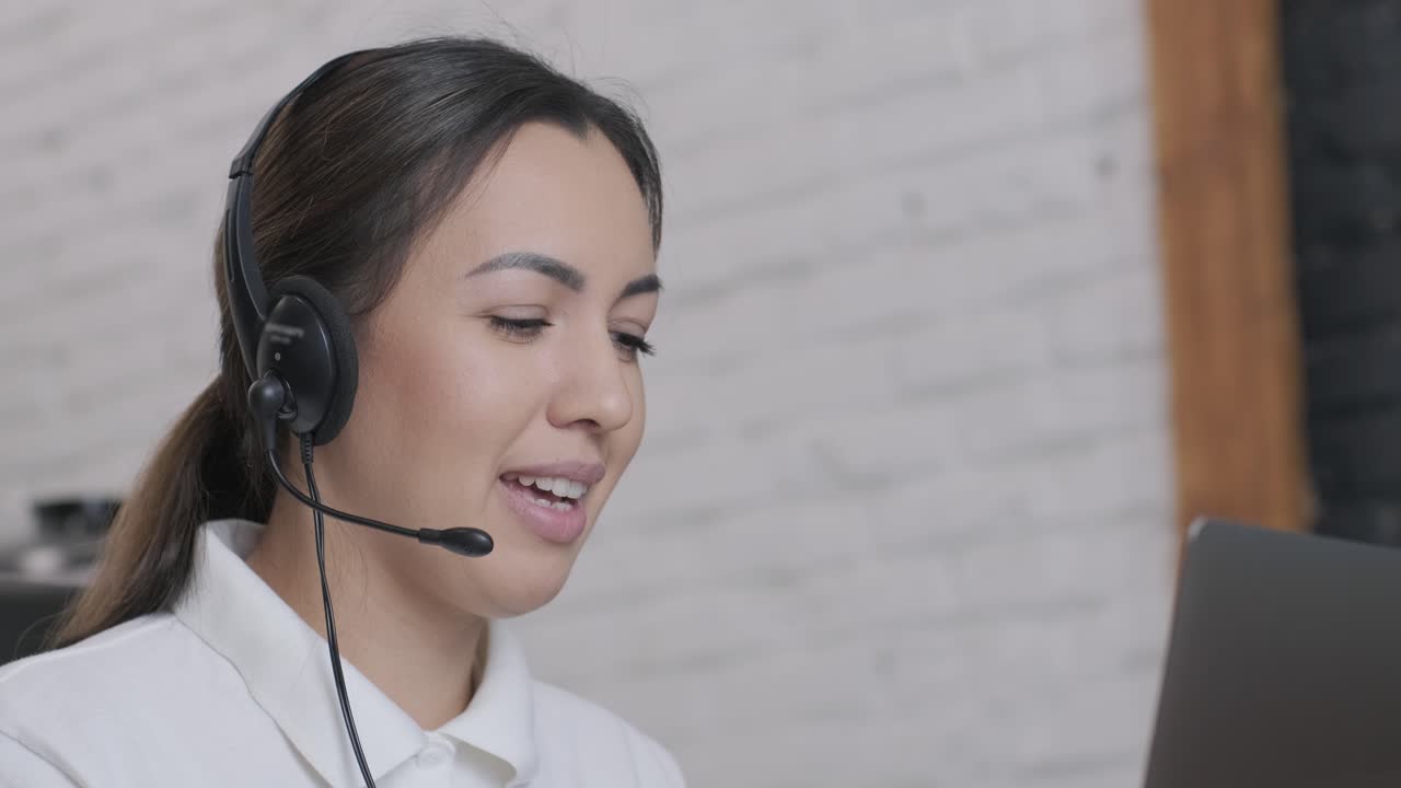 Smiling woman call centre operator, customer support agent wears headset consults client online typing on laptop, talk in internet computer chat, helpline operator secretary make conference video call