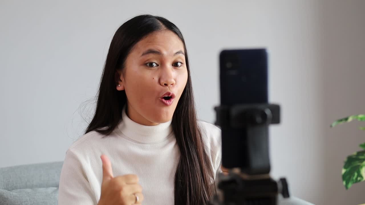 Giovane donna asiatica adulta che parla in diretta tramite la fotocamera selfie del cellulare, utilizzando un'app per l'assistenza alla salute mentale. Vlogger asiatica digitale virtuale che filma per la condivisione online.