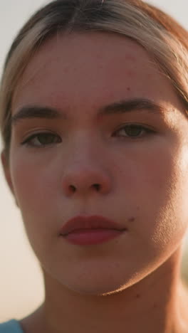 primer plano de una joven dama blanca con expresión de mal humor mirando directamente a la cámara, parpadeando los ojos bajo la cálida luz del sol, con efecto bokeh natural en el fondo