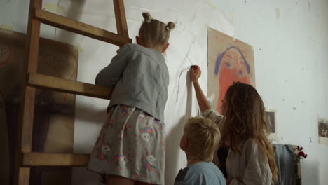 Back-view-of-female-painter-and-children-painting-on-wall-with-black-chalk.