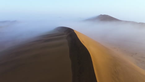 Aerial-view-over-fog-covered-sand-dunes,-sunny-morning-in-Namibia---reverse,-tilt,-drone-shot