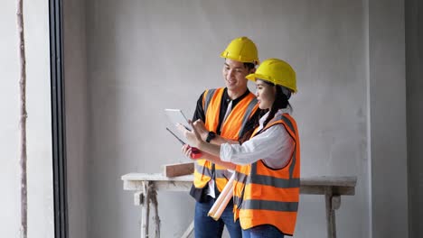 desde el trabajo en un sitio de construcción en el interior, una joven mujer y un capataz con chalecos naranjas y cascos de seguridad están haciendo llamadas de video en sus tabletas.