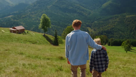 Back-view-father-son-walking-on-green-hill.-Parent-with-boy-going-down-slope.