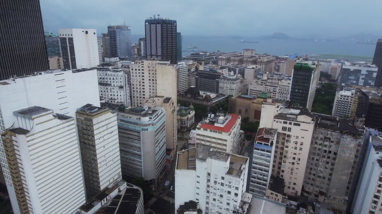 Vista aérea avançando sobre os arranha-céus do Rio, com o oceano visível ao fundo