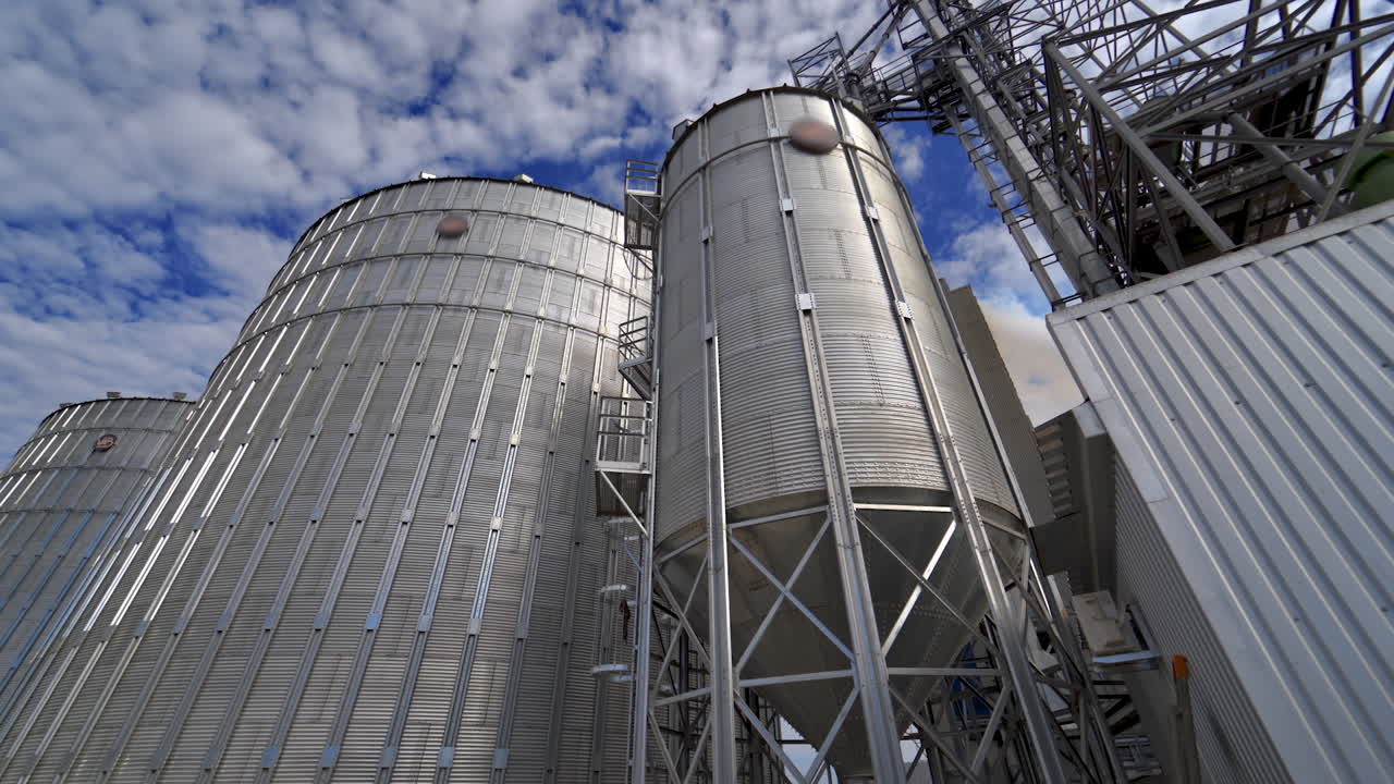Modern granary outdoors. Metallic elevators for storing grain. Agricultural complex with big aluminum containers under the blue sky.
