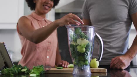 pareja de raza mixta poniendo verduras picadas en el frasco y dando cinco altos entre sí en casa