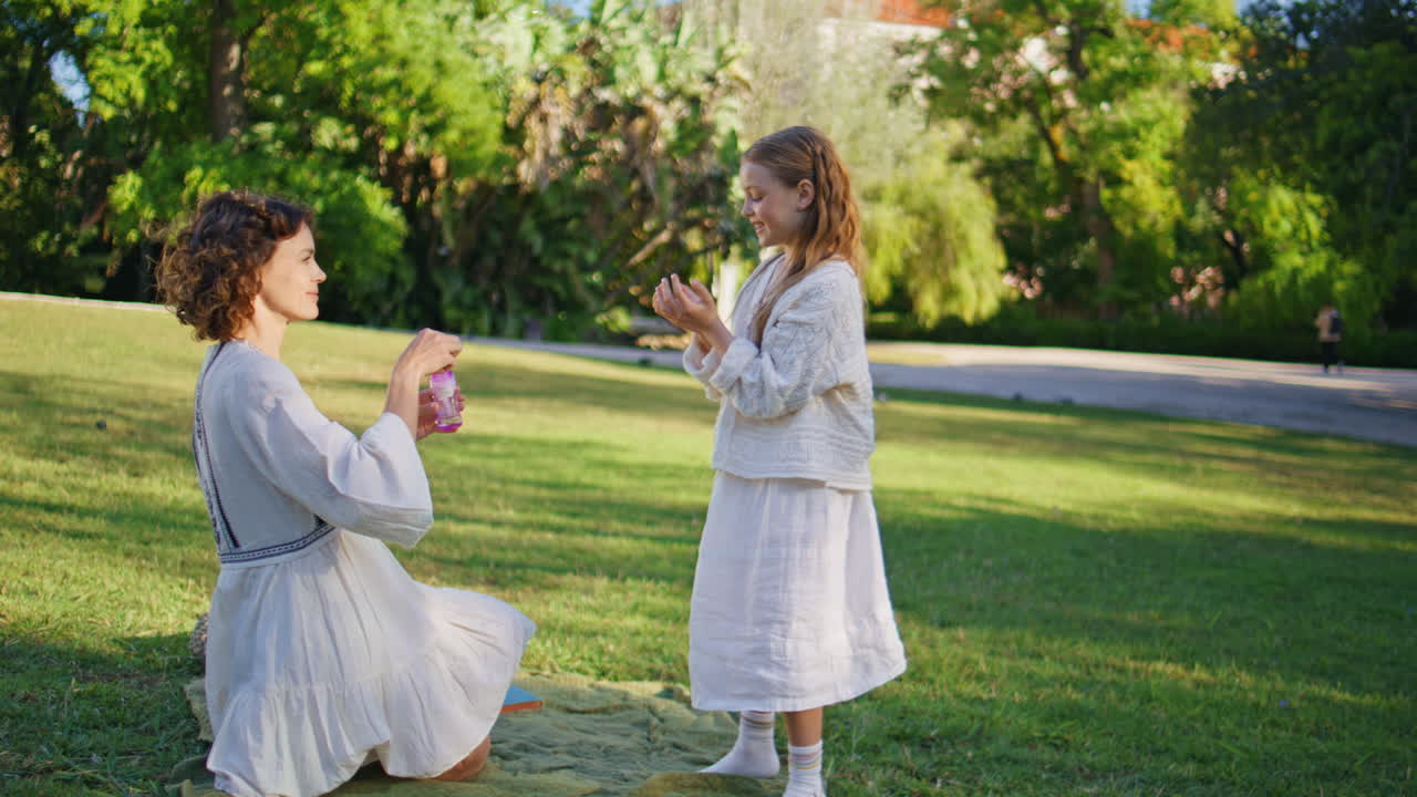 Mom child blowing soap colorful bubbles in green grass summer park together