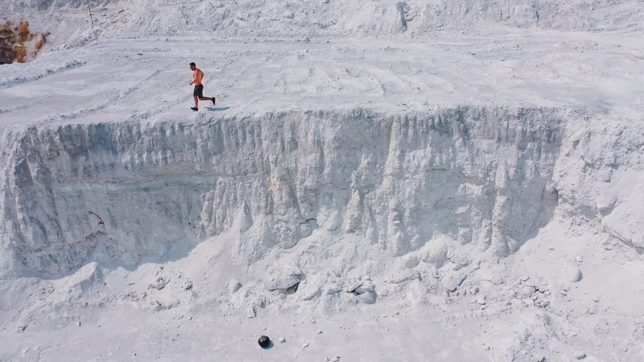 Sportsman on a white canyon. Healthy man in shorts doing his daily training outdoors. Strong athlete runs on the rocky hill in a sunny summer day. Aerial view.