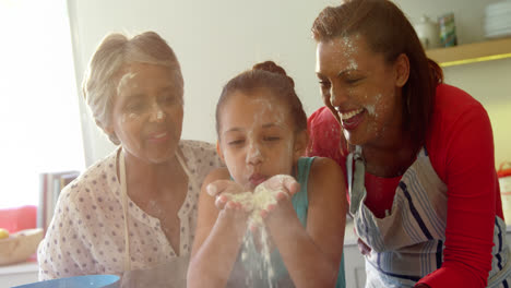 familia feliz de varias generaciones soplando harina en la cocina 4k