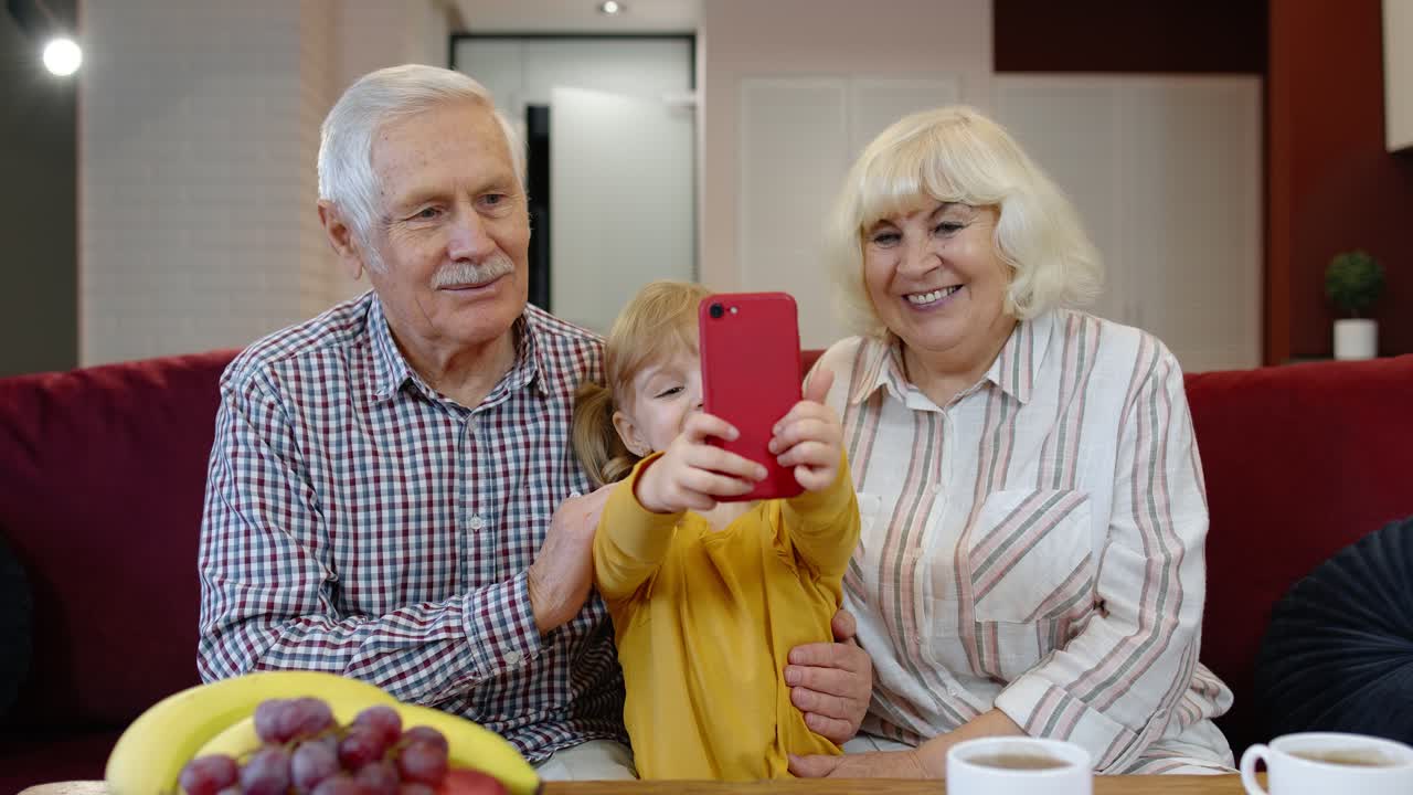 Ældre ægtepar bedsteforældre med barnebarn tager selfie-billeder sammen på mobiltelefon
