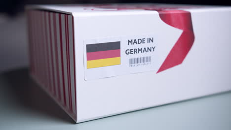 Manos-Aplicando-La-Etiqueta-De-La-Bandera-De-Alemania-En-Una-Caja-De-Cartón-De-Envío-Con-Productos