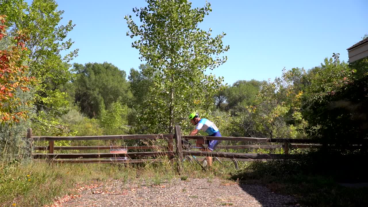A cyclist rides through a rustic wooden fence on a gravel path