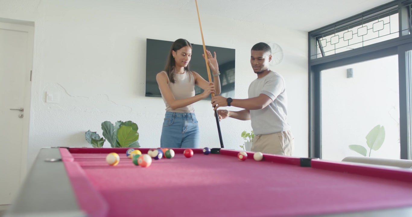 Couple practicing at home by red pool table while man holding cue upright teaching grip