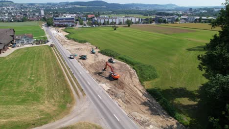 Excavator-shapes-road-expansion,-Swiss-city-in-backdrop