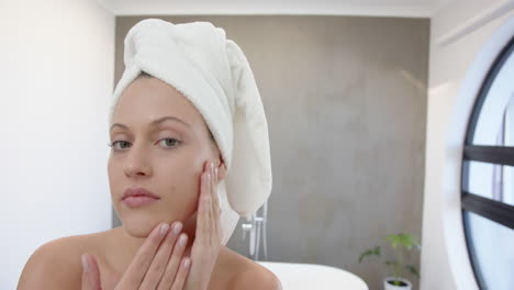 applying skincare, young woman with towel on head in spa bathroom, copy space
