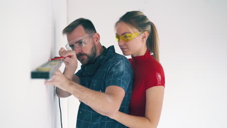 hombre con novia verifica el nivel de la pared en la habitación en la renovación