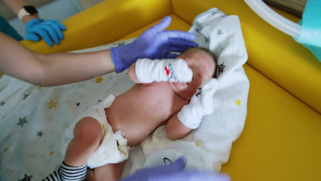 little baby lying on the yellow table is taken care by a nurse. medic undresses the newborn child.