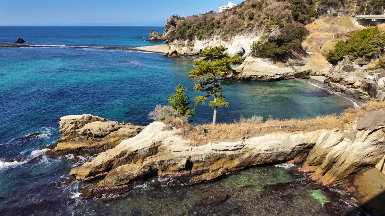 Una ripresa panoramica dall'alto che guarda giù sulle acque verde smeraldo e sulle scogliere bianche frastagliate di Dogashima, Giappone. La telecamera si inclina verso l'alto per rivelare un pino solitario appollaiato su un affioramento roccioso