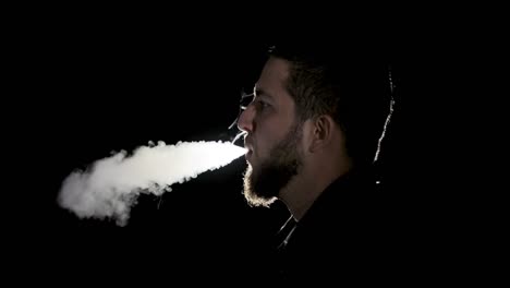 a young white bearded man in black shirt is vaping an electronic cigarette