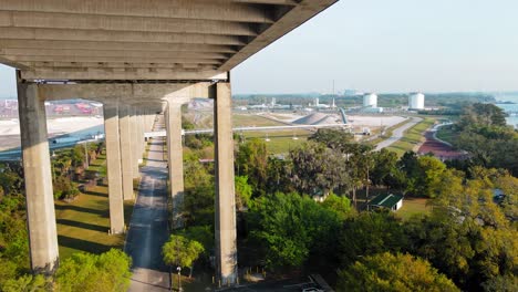 Volando-Un-Dron-De-4k-Debajo-De-Un-Puente-Con-Hermoso-Clima-Soleado-Y-Palmeras-En-Un-Clima-Tropical-Y-Camiones-Que-Transportan-Materias-Primas-Y-Productos-Básicos-Al-Puerto-Marítimo