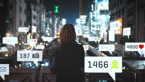 young woman with her back to the camera looking at bright lights of a big city with its advertising banners at night