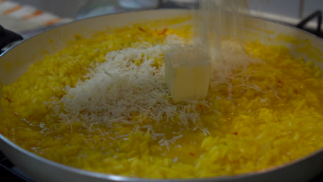 chef adding butter and freshly grated parmesan cheese to a yellow saffron risotto