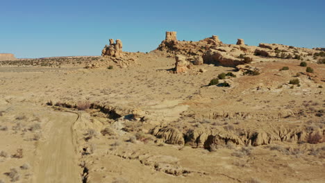 Aerial-of-car-on-rugged-desert-road-passing-by-hoodoo-rock-formations,-4K