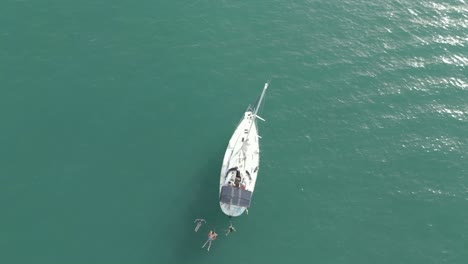 young people swimming and having fun in the sea next to their sailing boat