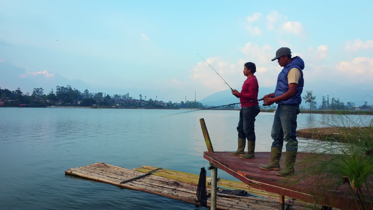 Two Friends Standing On Wooden Dock And Enjoying Peaceful Fishing Trip At Beautiful Lake