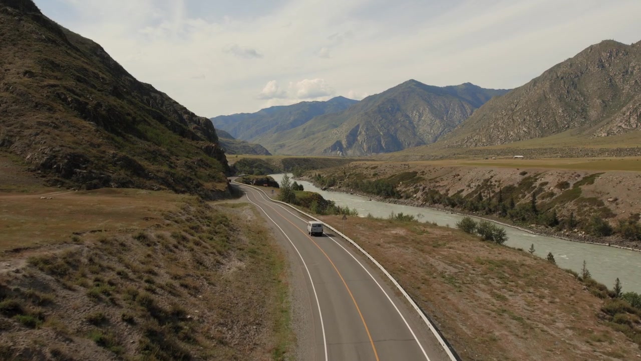Metraje de dron de una sinuosa carretera Chuysky Trakt que discurre junto al río Katun de color turquesa a través de un amplio valle de montaña en la República de Altai, Rusia, en un día nublado.