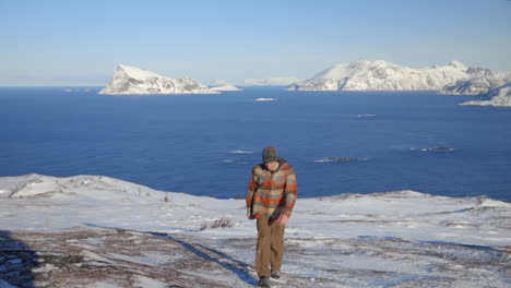 a man hiking up a snowy landscape with the arctic ocean and mountains in the background, slow motion