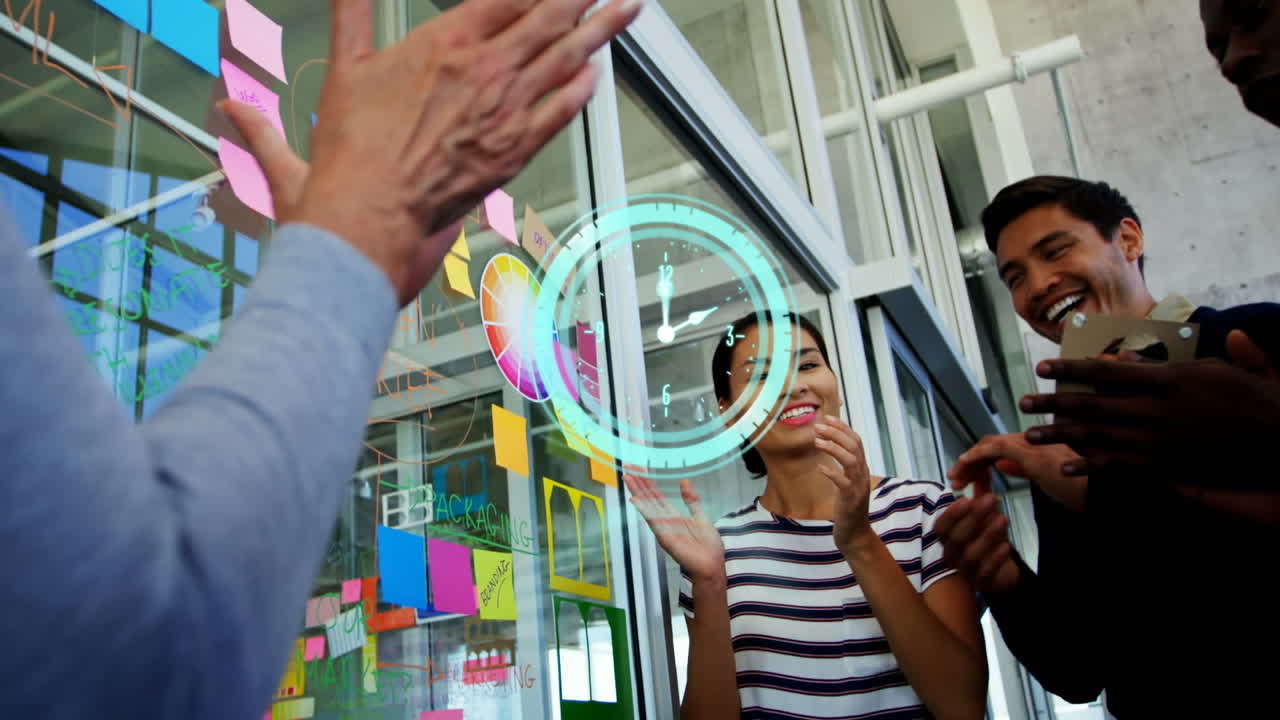 Animation of clock over diverse male and female business colleagues brainstorming and clapping hands